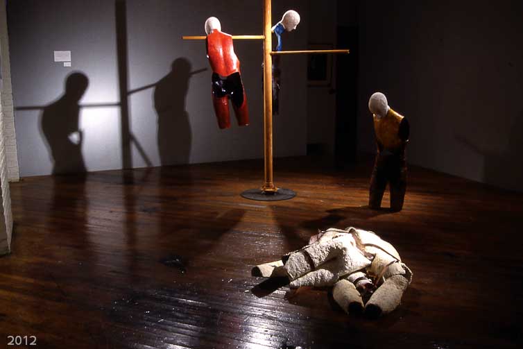 A mixed media grouping, whose materials include: fiberglass, burlap, satin, leather, acrylic paint, wax, and leather. This installation grew out of a scene in a novel by Michael Ondatje called "In the Skin of a Lion". The scene dealt with immigrants who worked in a tannery dying leather in the early 1900’s in Ontario, Canada. The skin dyers would take hides fresh from the slaughterhouse and bring them to cisterns in the ground filled with dyes. They then beat the dye into the skins. When they finished, the skin dyers emerged from the vats covered in dye up to their necks. While the dye could be washed away, the smell never left them, and the chemicals they were exposed to lead to illness and early death. 